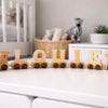 Wooden toy train with letters spelling 'LOULE' on a white surface in a nursery.