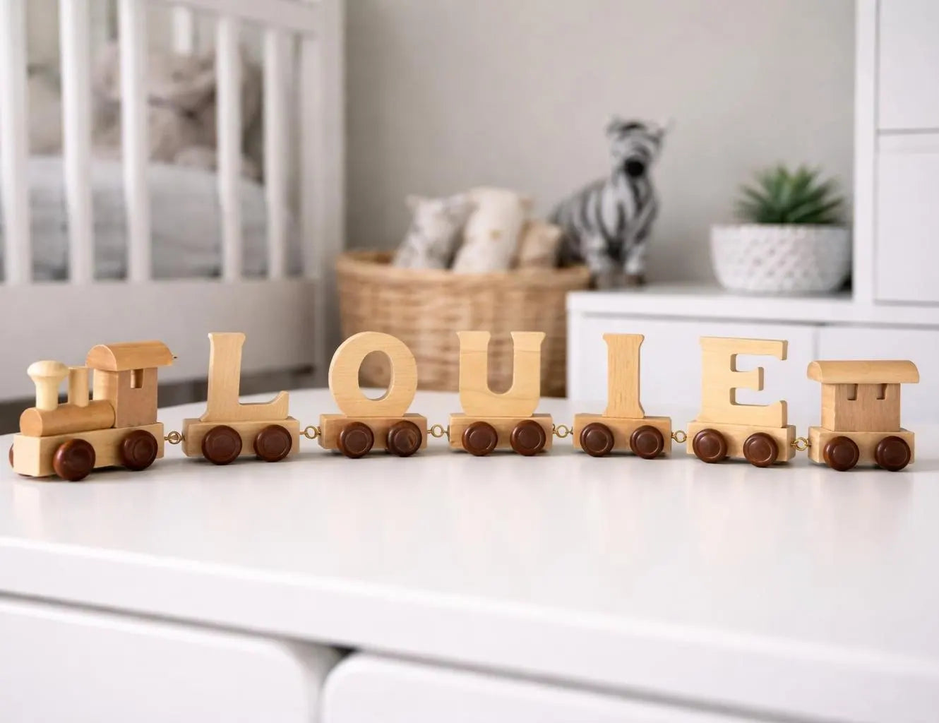Wooden toy train with letters spelling 'LOULE' on a white surface in a nursery.